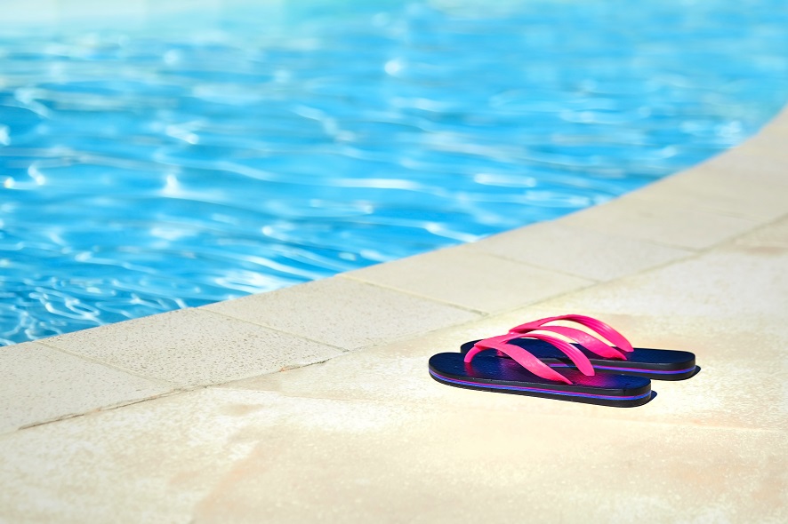 Pink flip flops near the swimming pool with blue water. Summer resort. Beach shoes